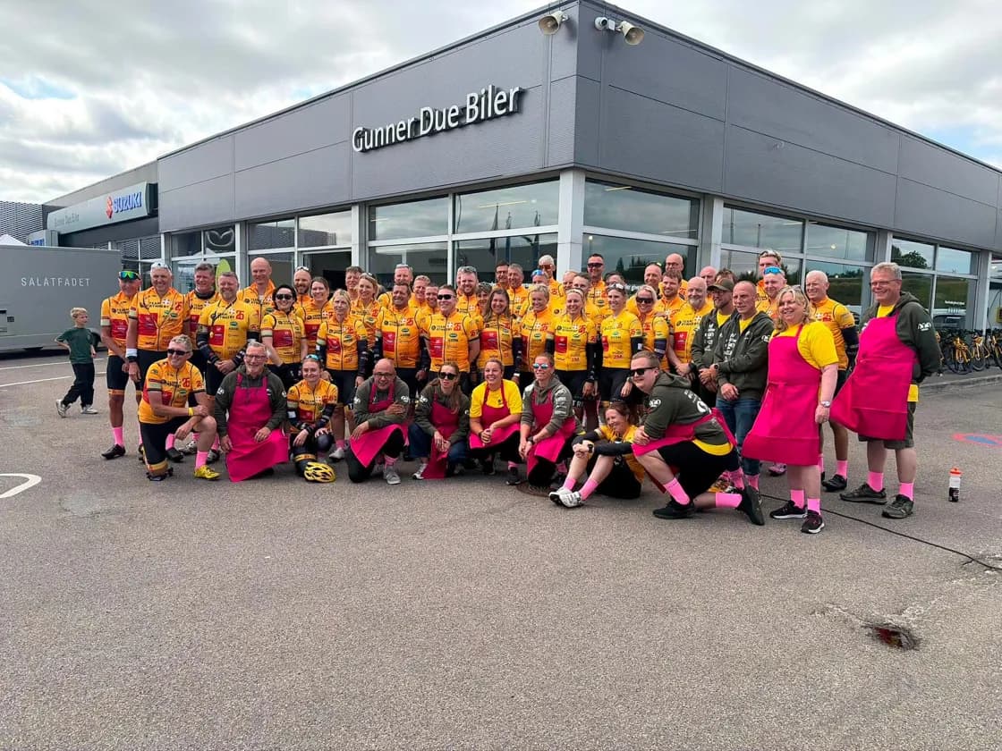 A Team Rynkeby team and its helpers in pink aprons posing outside a local business