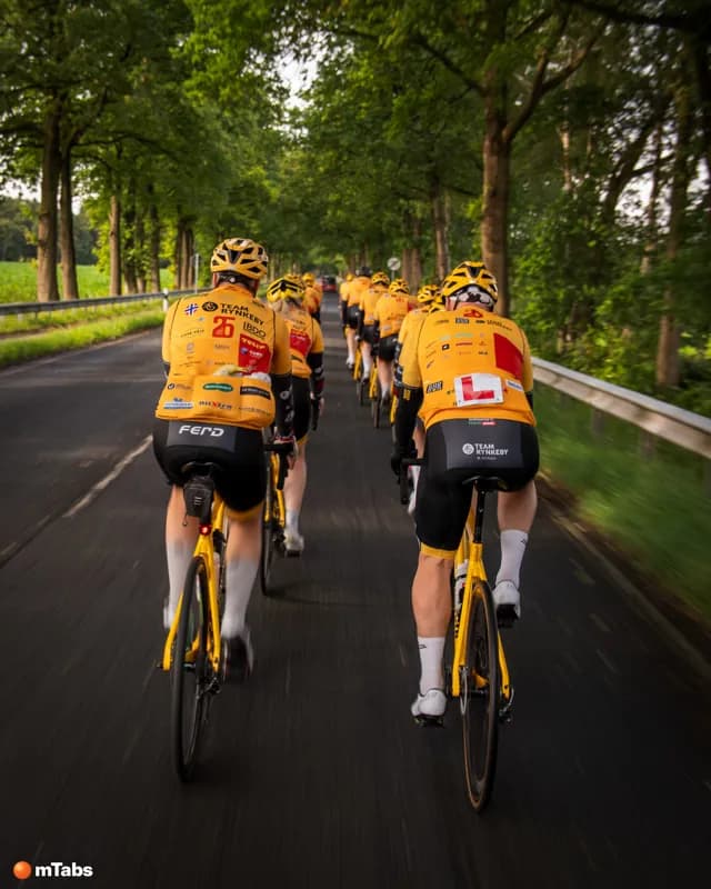 Team Rynkeby riders in a long line down a tree-lined road