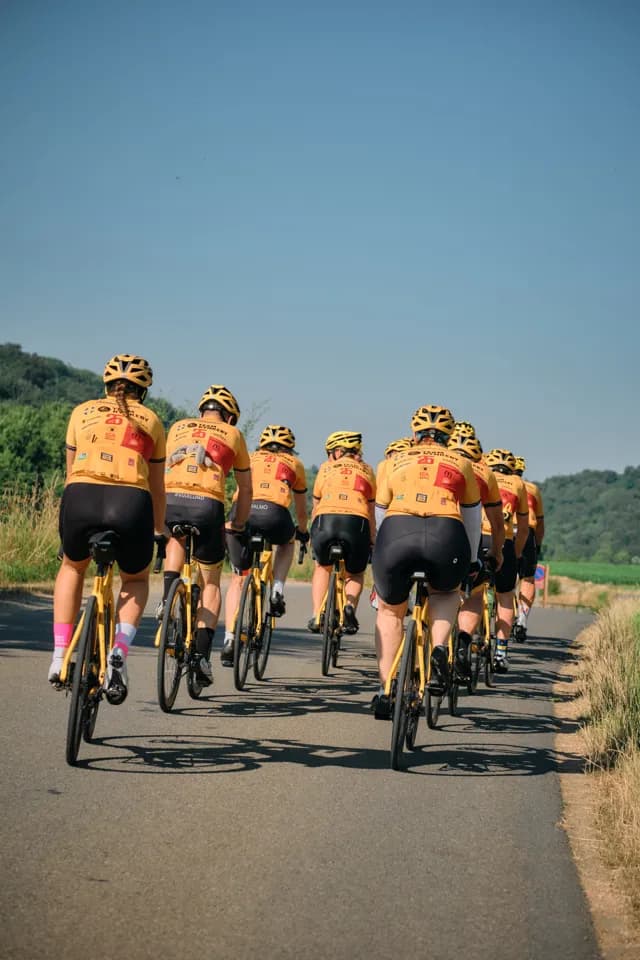 Team Rynkeby riders seen from behind, riding together under a blue sky