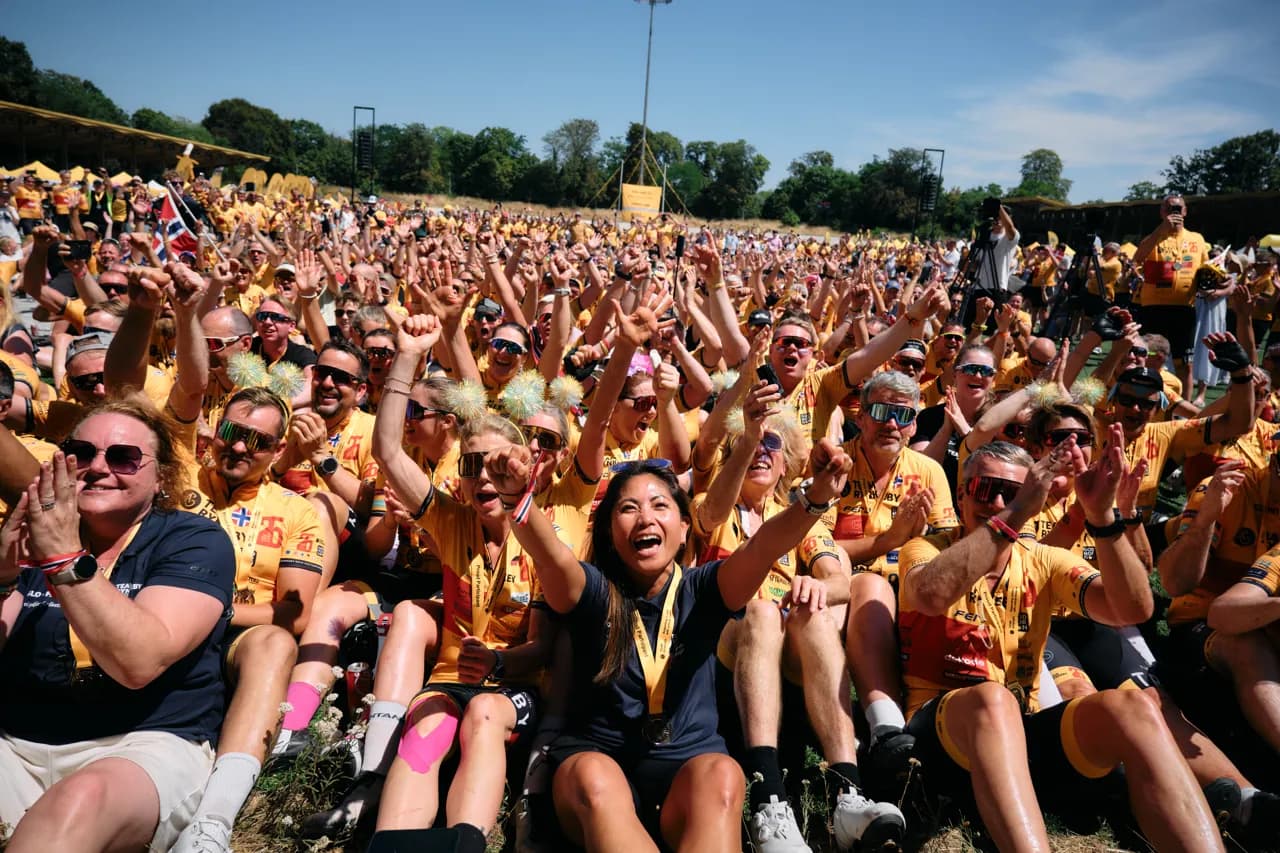 Hundreds of riders in yellow jerseys cheering with their arms in the air